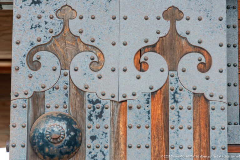 Two mirrored dark metal ornaments with curved tops mounted on a studded wooden gate.