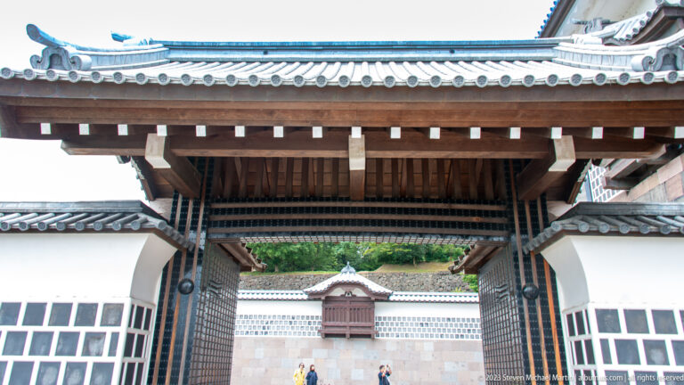Timber castle gate framing a white inner wall and smaller projecting window beyond.