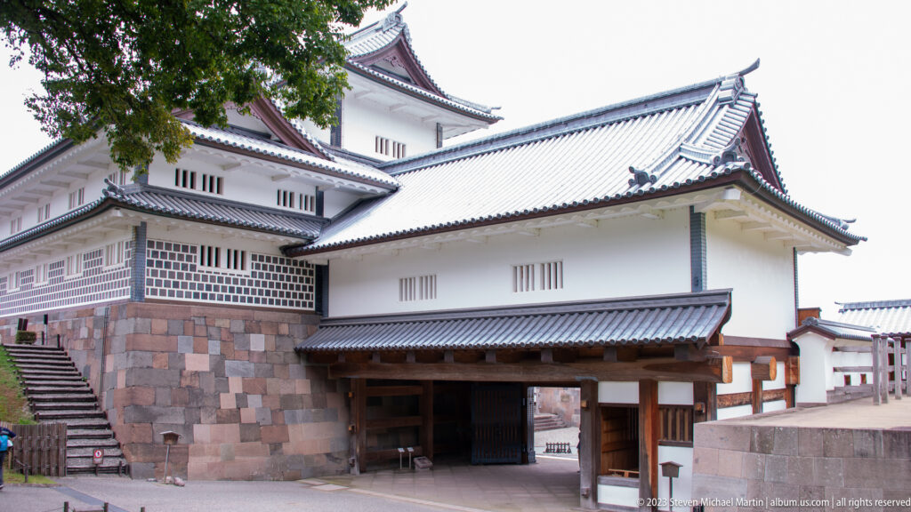 Kanazawa Castle gate complex with stairs, stone base, white walls, and tiled upper turret.