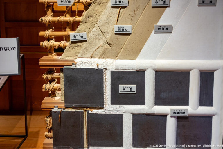 Stepped display of coarse earth, dark base layers, and progressively smoother white plaster wall samples with labels.