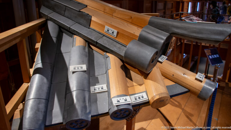 Full-scale display of timber beams, projecting eaves, and gray curved roof components with individual labels.