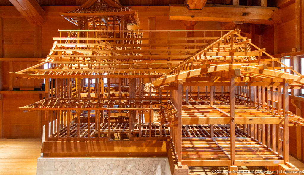 Large wooden structural model showing connected castle buildings, roof trusses, posts, corridors, and stone-faced bases.