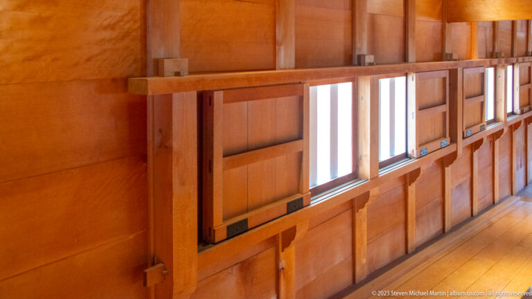 Close interior view of timber wall framing with narrow rectangular windows, horizontal rails, and exposed joinery.