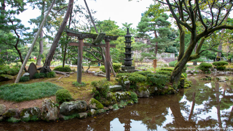 Torii and multi-tiered stone pagoda stand beside a shallow pond among mossy rocks and clipped shrubs.