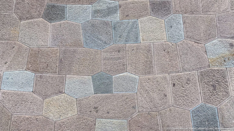Close view of tightly fitted polygonal stone slabs in muted pink, gray, blue, tan, and brown.