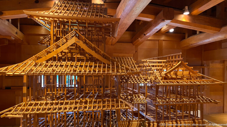 Large wooden architectural model reveals posts, beams, rafters, and layered roofs inside a timber gallery.