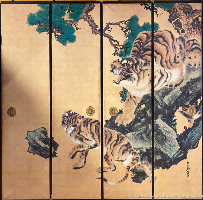 Gold folding screen painted with an adult tiger and cubs among rocks and dark pine branches.