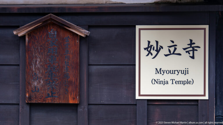 Bilingual Myōryū-ji “Ninja Temple” sign beside an older inscribed wooden plaque on a dark timber wall.