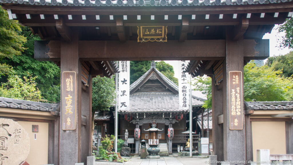 Wooden Buddhist temple gate frames a tiled worship hall and incense burner beyond.