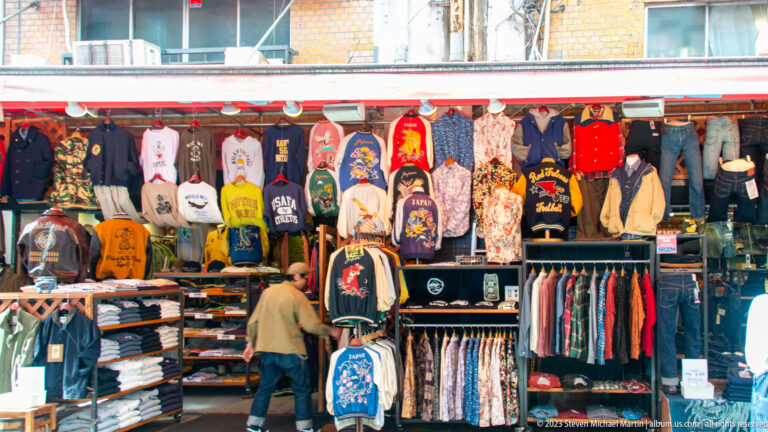 Market clothing stall filled with embroidered jackets, T-shirts, racks, and folded garments.
