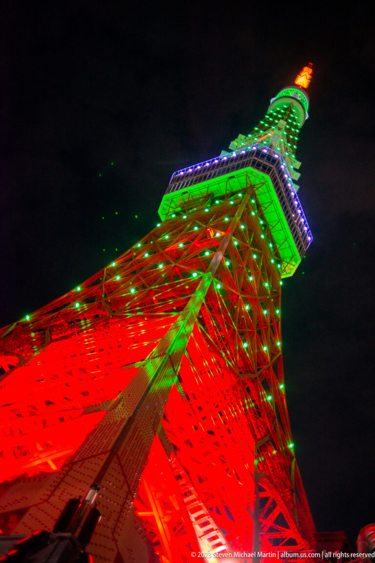 Oblique upward view of Tokyo Tower’s red steel lattice and green illuminated top.
