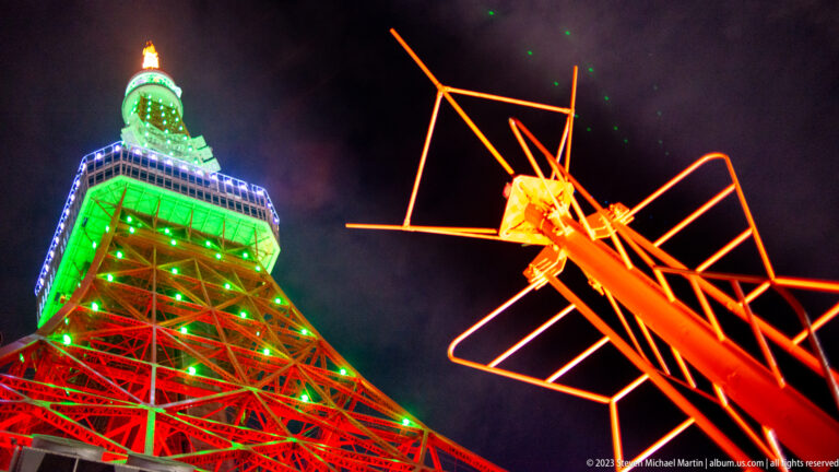 Tokyo Tower behind a bright orange insect-like metal sculpture at night.