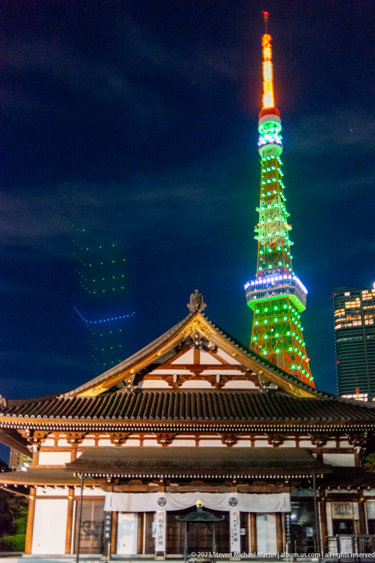 Tokyo Tower glowing behind the tiled roof of a Zōjō-ji temple building at night.