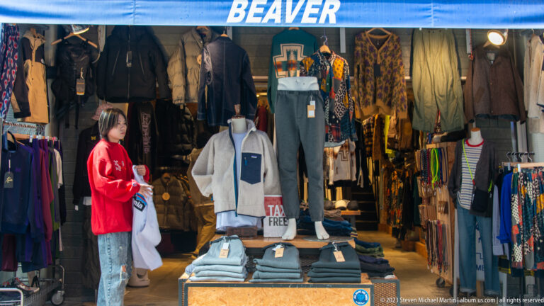 Beaver clothing storefront with mannequins, hanging jackets, folded pants, and a staff member.