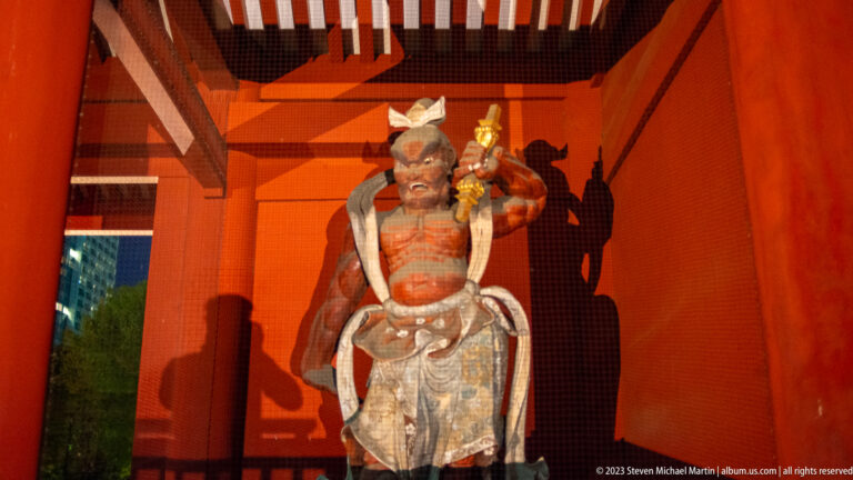 Wooden Niō guardian statue holding a ritual weapon inside a red temple gate.
