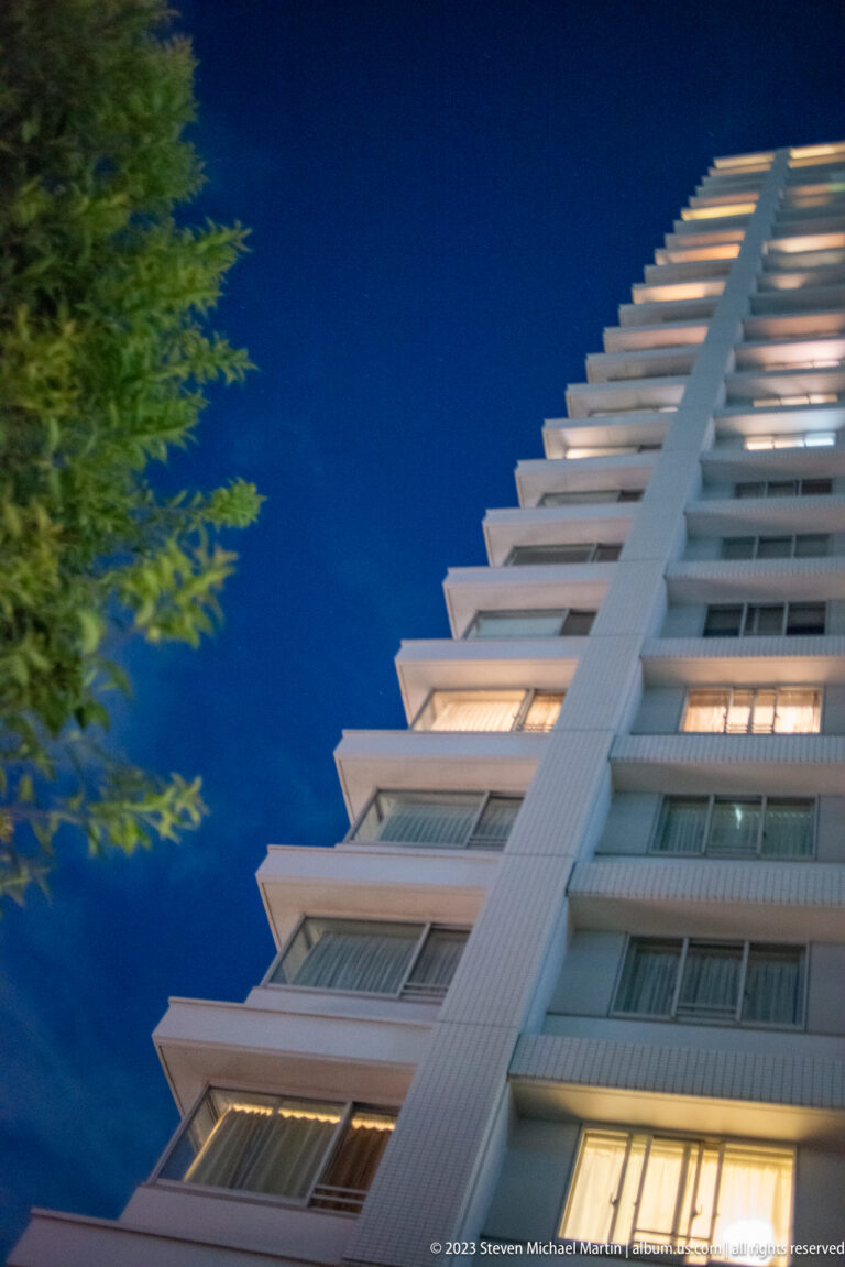 Low-angle night view of a modern high-rise with stacked balconies and lit windows.