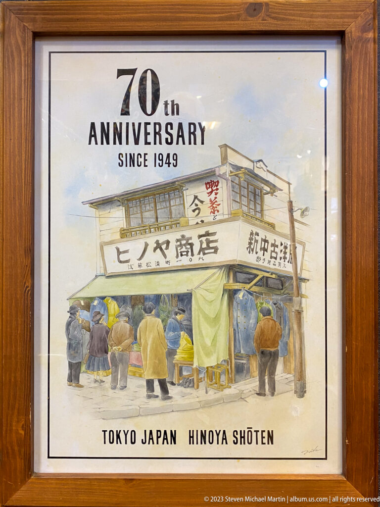 Framed Hinoya Shōten 70th anniversary illustration showing a storefront and customers.