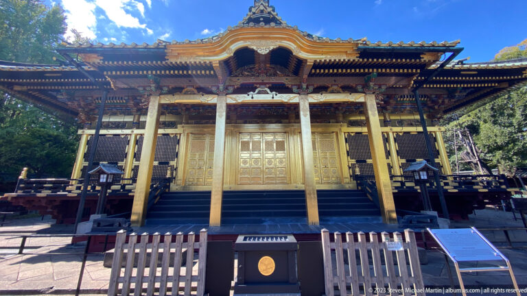 Frontal view of Ueno Tōshōgū with gilded doors, carved gable, steps, and fenced forecourt.
