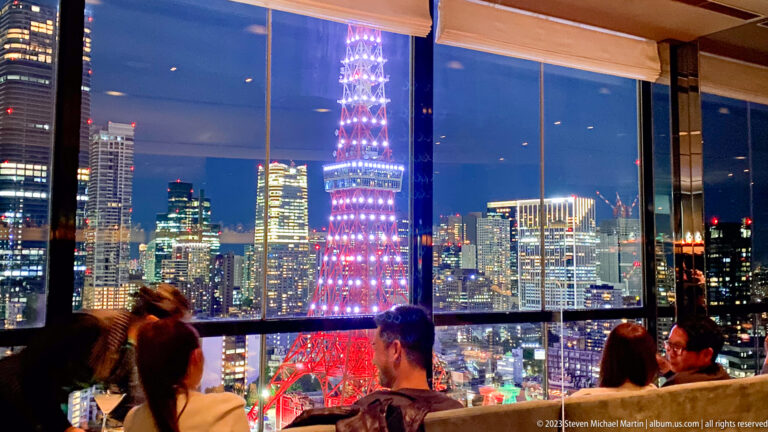 Tokyo Tower glows beyond large lounge windows while seated guests face the night skyline.