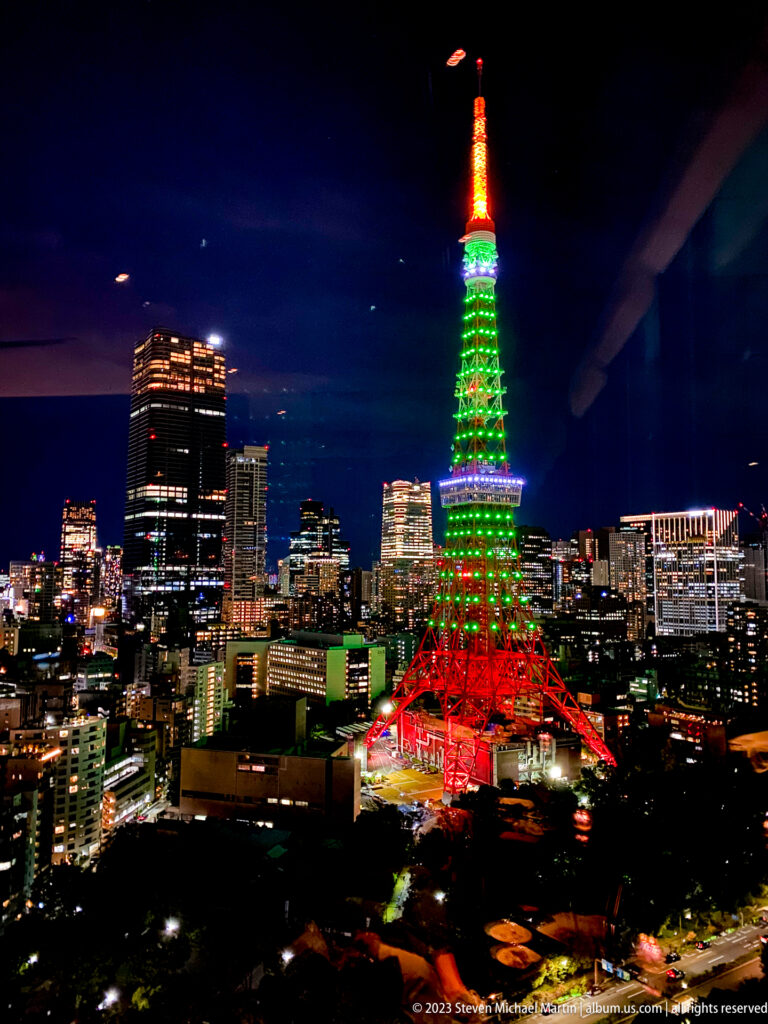 Wide night panorama with Tokyo Tower glowing red, green, and orange above the city.