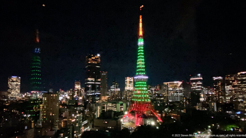 Distant Tokyo Tower glows above dense buildings in an elevated night view.