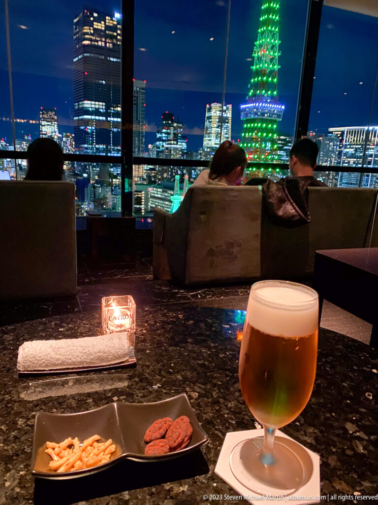 Beer and snacks on a lounge table with Tokyo Tower glowing beyond seated guests.