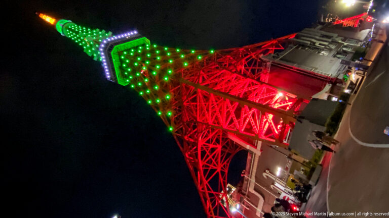 Rotated low-angle view up Tokyo Tower’s red lattice toward its green upper section.