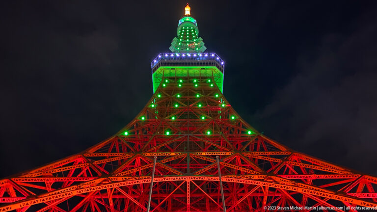 Symmetrical upward view of Tokyo Tower’s red lattice and green observation deck.