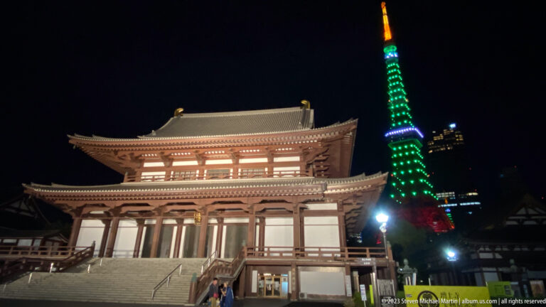 Illuminated Zōjō-ji temple hall with Tokyo Tower rising behind at night.