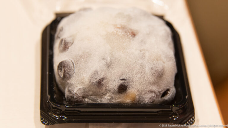 Close-up of a dark rounded Japanese sweet heavily dusted with pale powder in a black tray.