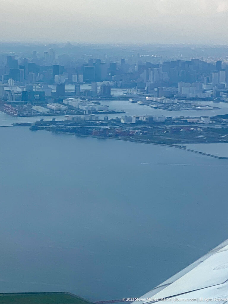 Aerial view of Tokyo waterfront with docks, waterways, industrial buildings, and aircraft wing.