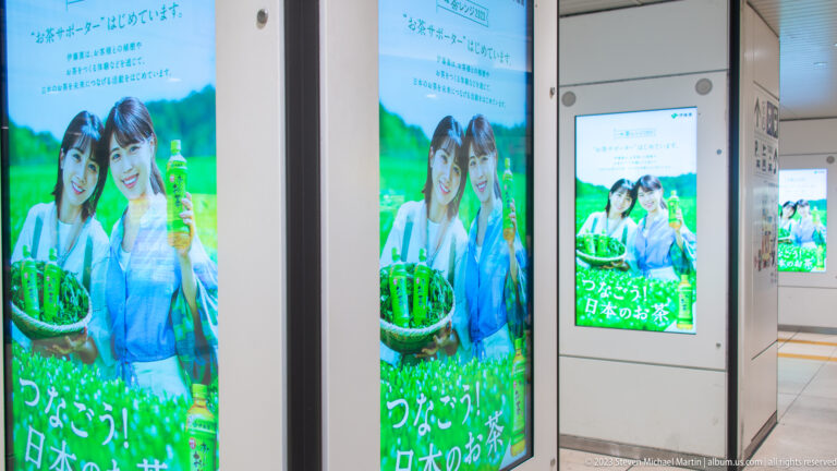 Multiple station screens repeat an advertisement of two women holding a basket of green produce.