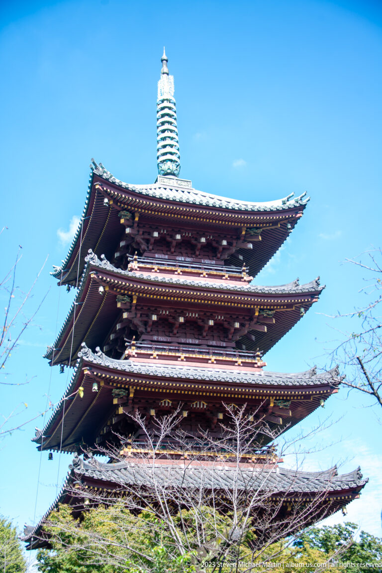 Close view of pagoda tiers with dark tiled eaves and a tall finial against blue sky.