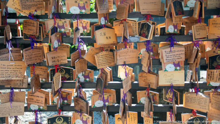 Rows of wooden ema prayer plaques with handwritten messages and colorful cords at a Shinto shrine.