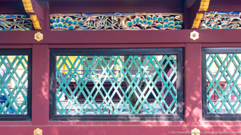 Turquoise diagonal lattice windows beneath colorful carved flowers in a red shrine wall.