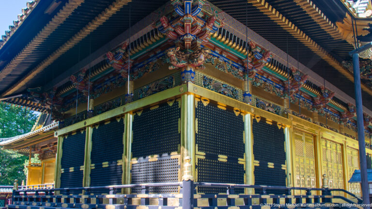 Oblique corner of a shrine hall with painted brackets, gilded posts, dark lattice panels, and deep eaves.