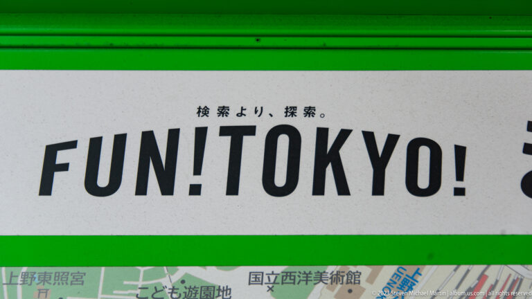 Green-and-white sign reads “FUN! TOKYO!” above Japanese text and part of a transit map.
