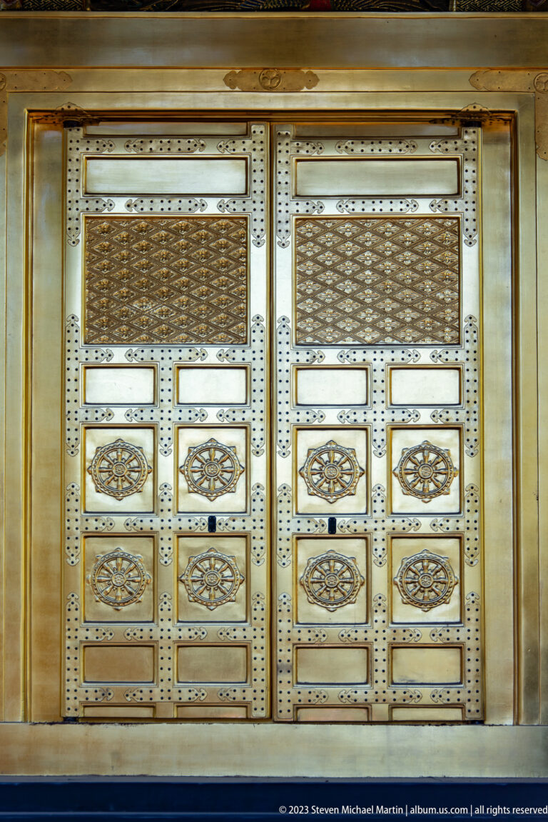 Close frontal view of gilded double doors with metal studs, floral bosses, and patterned grilles.