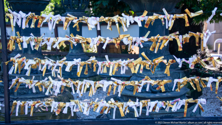 Many white and gold paper fortune slips tied in rows across cords at a shrine.