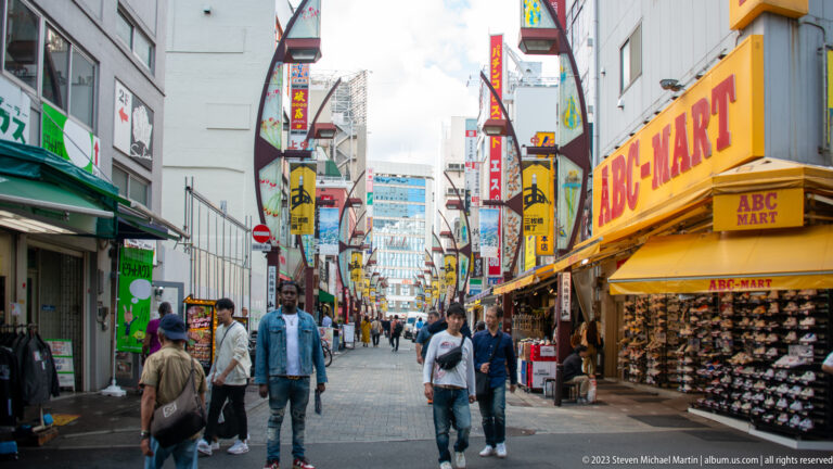 Busy pedestrian street with a large yellow ABC-MART shoe store and many vertical signs.