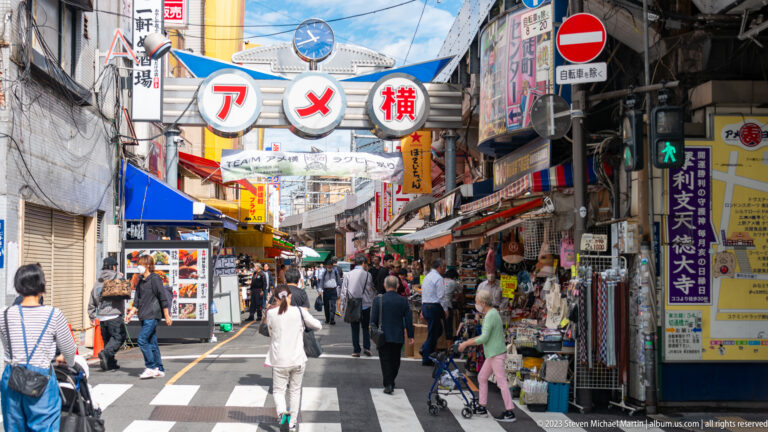 Shoppers enter Ameyoko beneath its arched sign on a narrow street lined with market stalls.