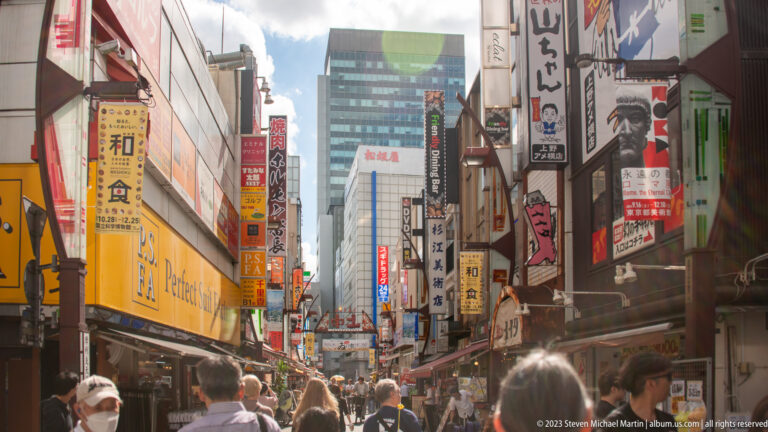 Backlit crowd fills a narrow Tokyo shopping street lined with tall signs and storefronts.