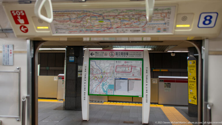 Tokyo subway platform with route maps, neighborhood information board, platform doors, and yellow tactile paving.