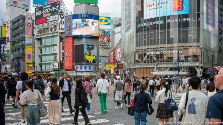 Pedestrians cross Shibuya beneath large screens beside the curved Tsutaya and Starbucks building.