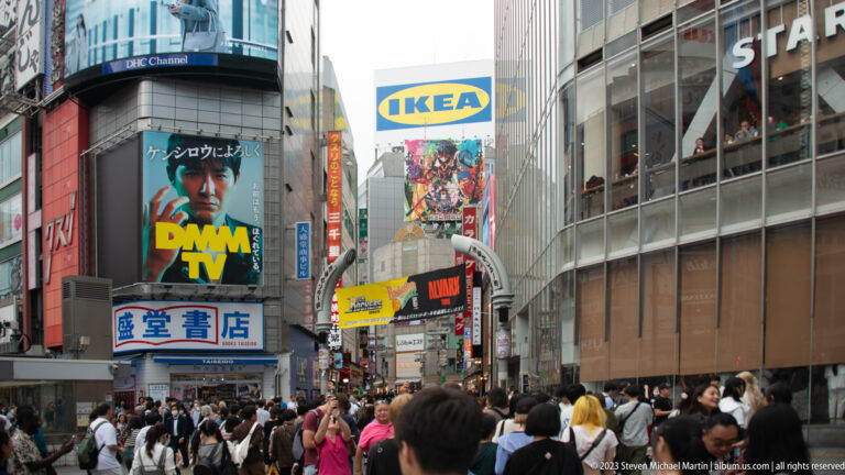 Heavy pedestrian crowd beneath IKEA and entertainment signs near Shibuya Crossing.