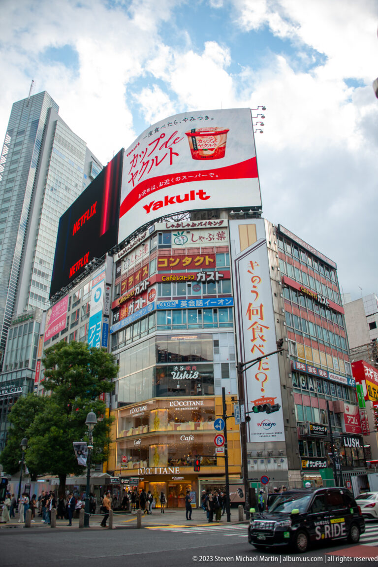 QFRONT building with Netflix and Yakult screens above shops and traffic at Shibuya Crossing.