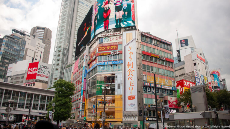 Commercial towers with giant screens and dense signs rise above Shibuya Crossing.