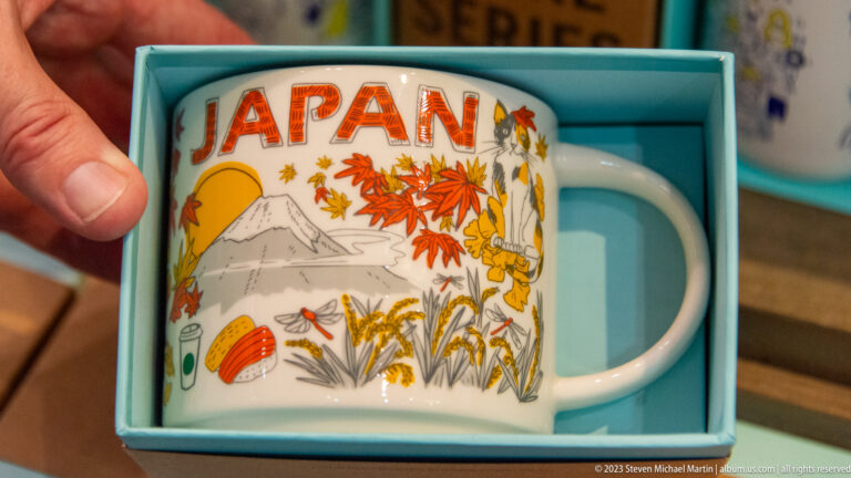 White souvenir mug in a blue box decorated with Mount Fuji, maple leaves, birds, and the word Japan.
