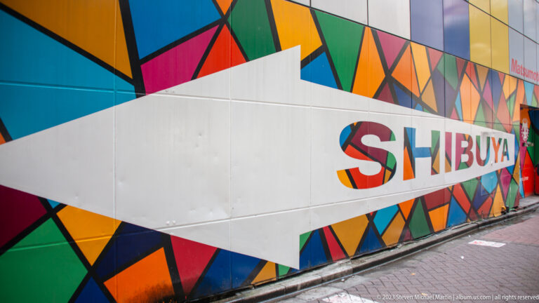 Long geometric mural on a construction wall with multicolored letters spelling Shibuya.