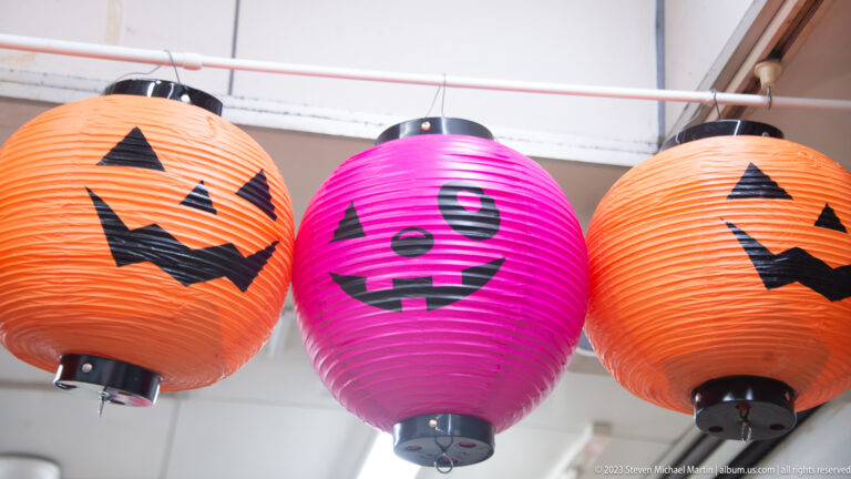Two orange and one magenta paper lantern hang with black jack-o’-lantern faces.